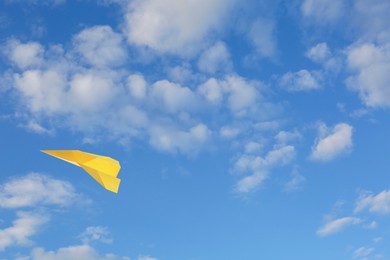 Image of Yellow paper plane flying in blue sky with clouds