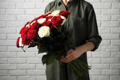Woman holding luxury bouquet of fresh roses near white brick wall, closeup