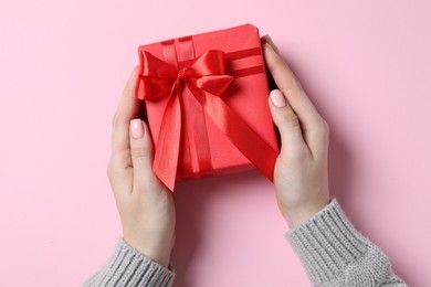 Christmas present. Woman holding gift box on pink background, top view