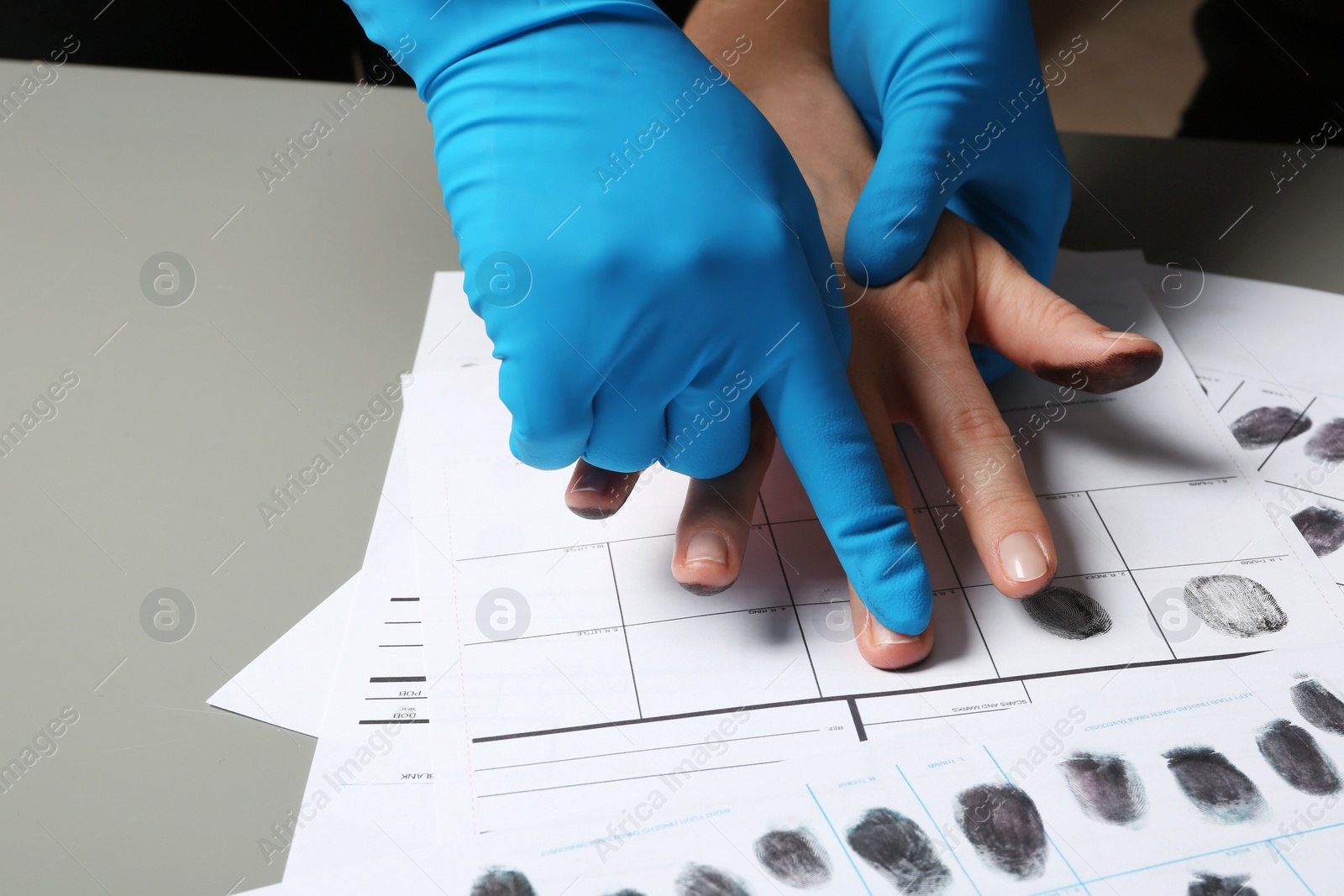 Photo of Investigator taking fingerprints of suspect on table, closeup