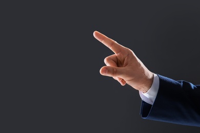 Photo of Businessman touching empty virtual screen against dark background, focus on hand