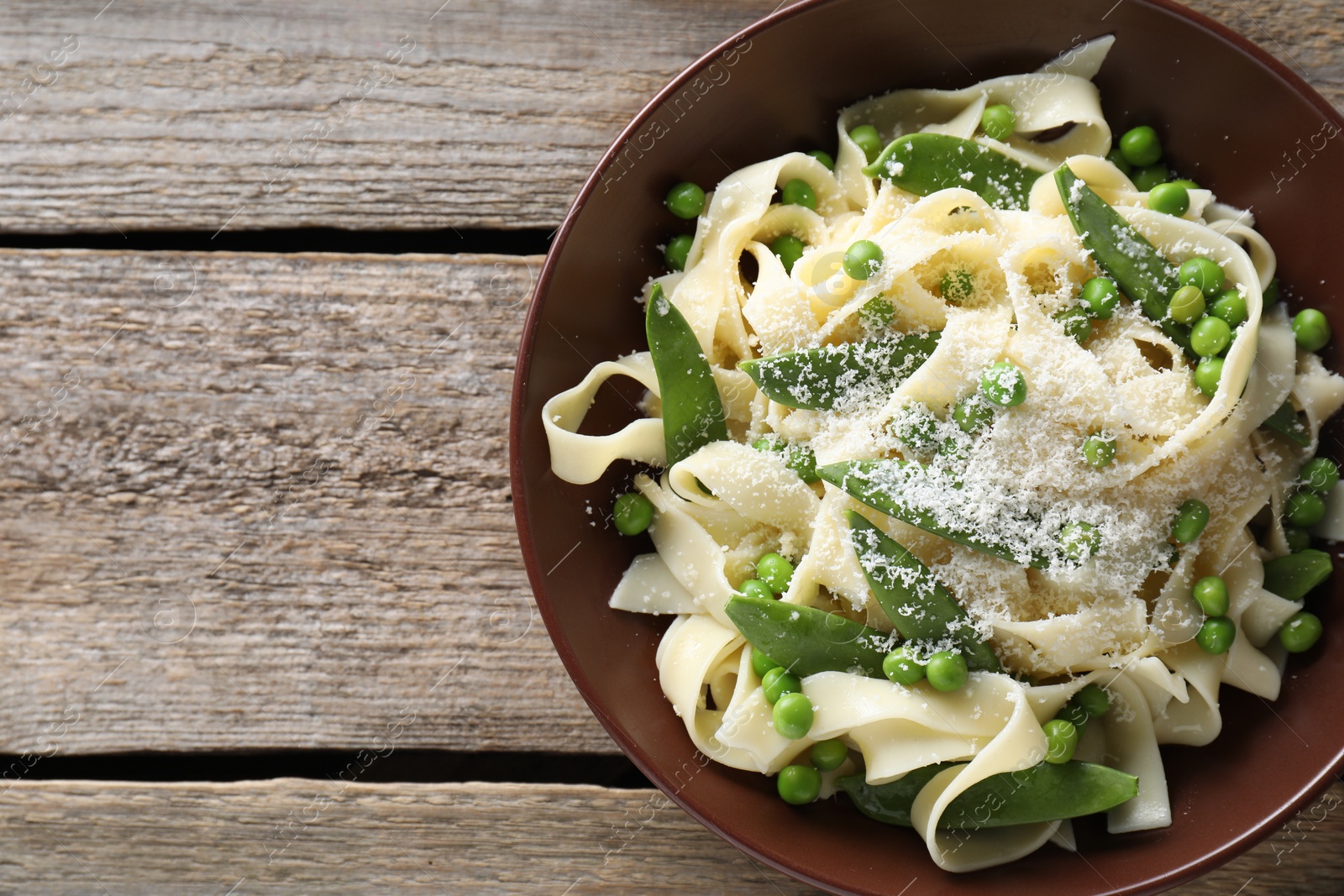 Photo of Delicious pasta with green peas and cheese on wooden table. Space for text