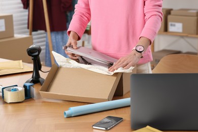 Photo of Seller packing bag into cardboard box at table in office, closeup. Online store