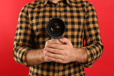 Photo of Young man with vintage video camera on red background, closeup