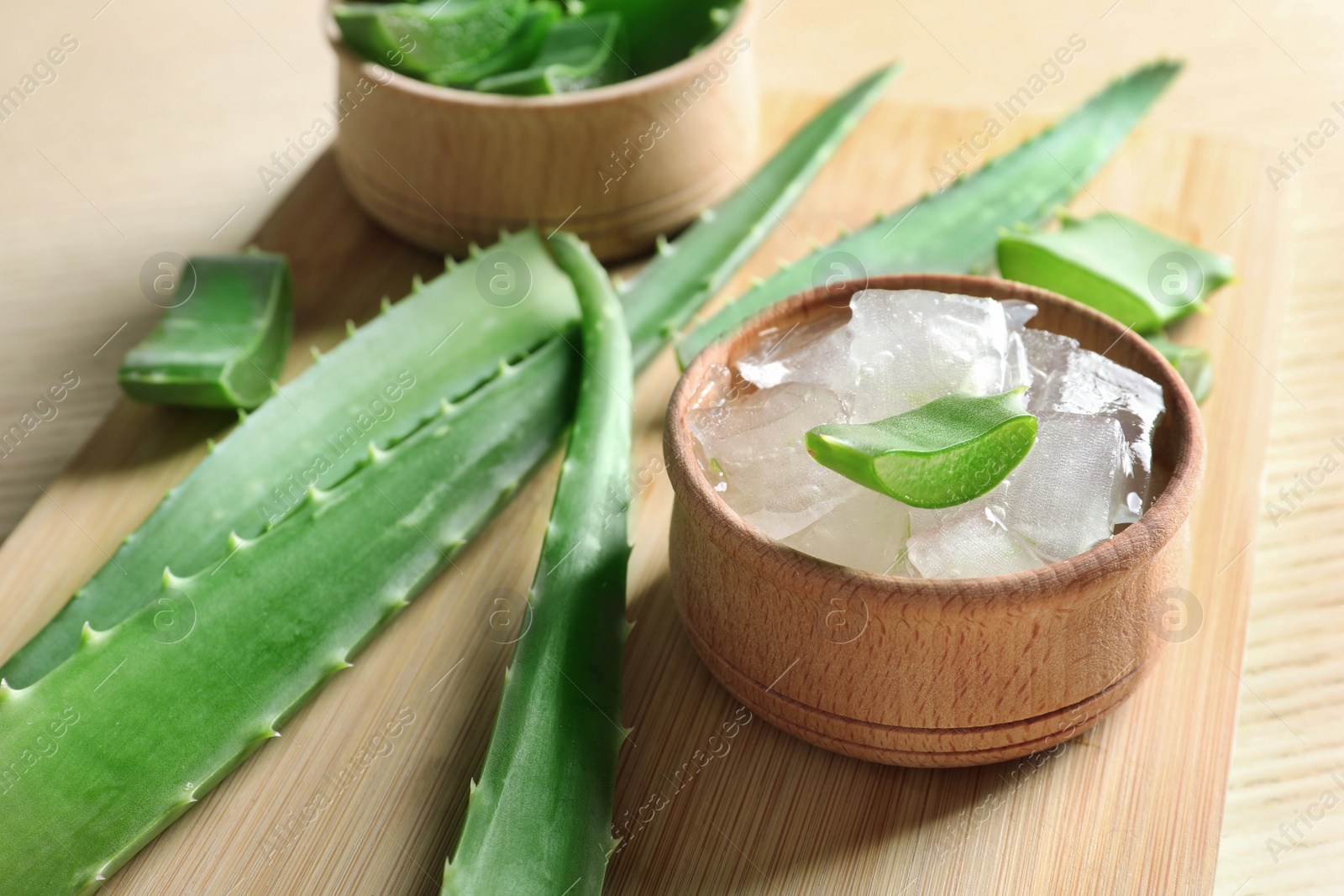 Photo of Bowl with peeled aloe vera and green leaves on wooden board