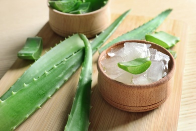 Photo of Bowl with peeled aloe vera and green leaves on wooden board