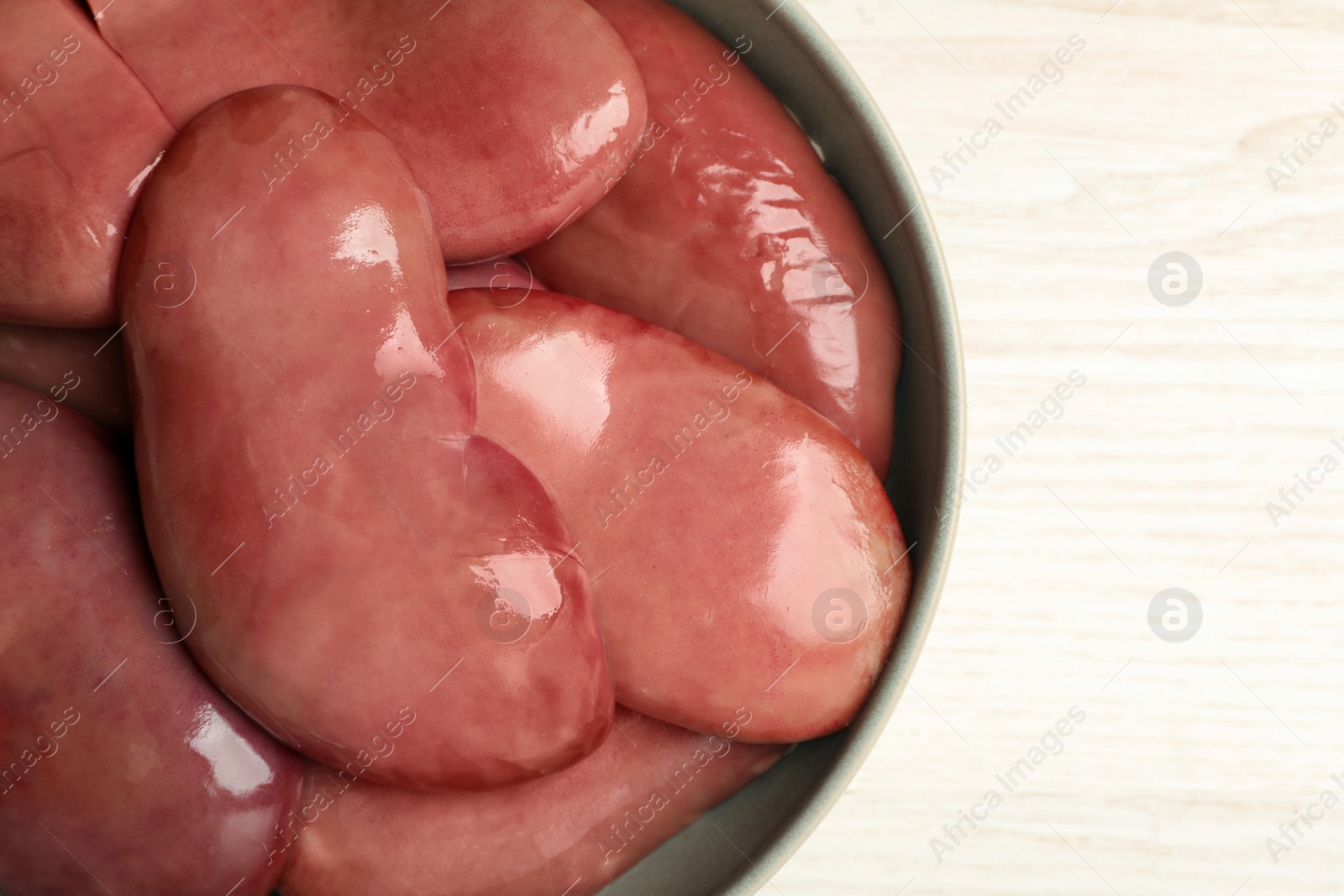 Photo of Bowl with fresh raw pork kidneys on white wooden table, top view. Space for text