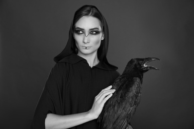 Photo of Mysterious witch with raven on dark background. Black and white effect