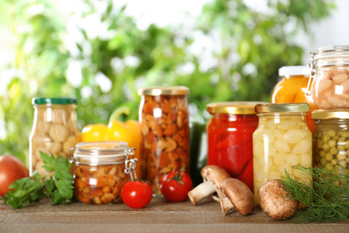 Photo of Glass jars of different pickled vegetables on wooden table