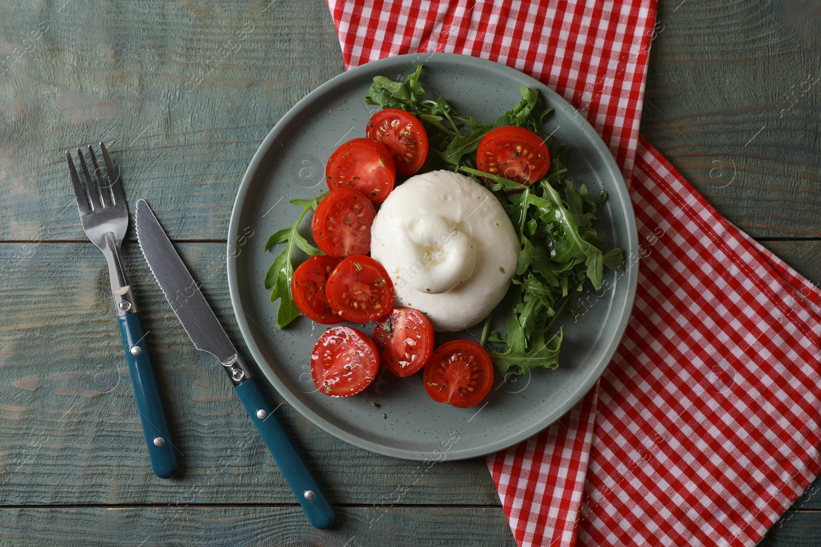 Photo of Delicious burrata cheese with tomatoes and arugula served on grey wooden table, flat lay