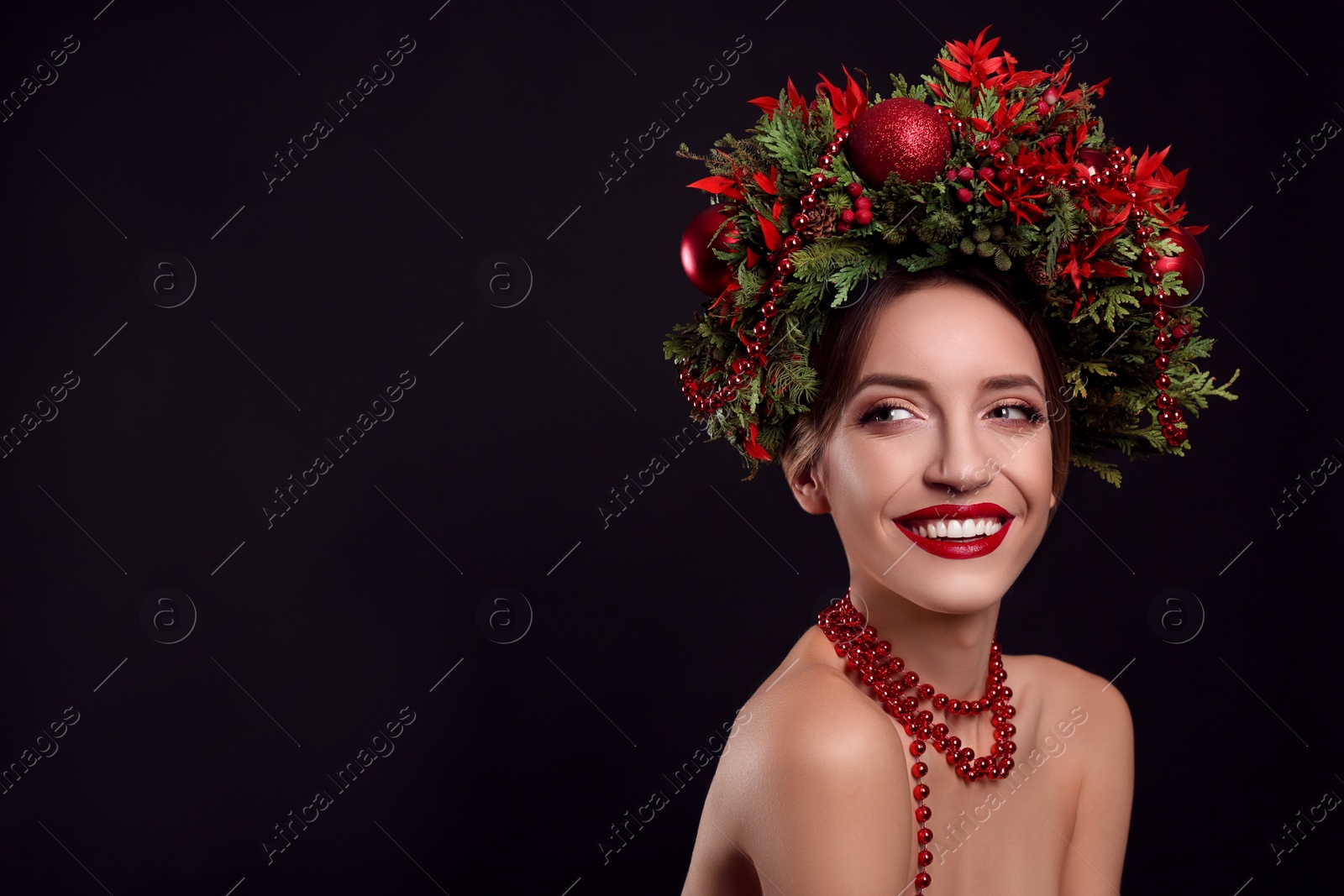 Photo of Beautiful young woman wearing Christmas wreath on black background. Space for text