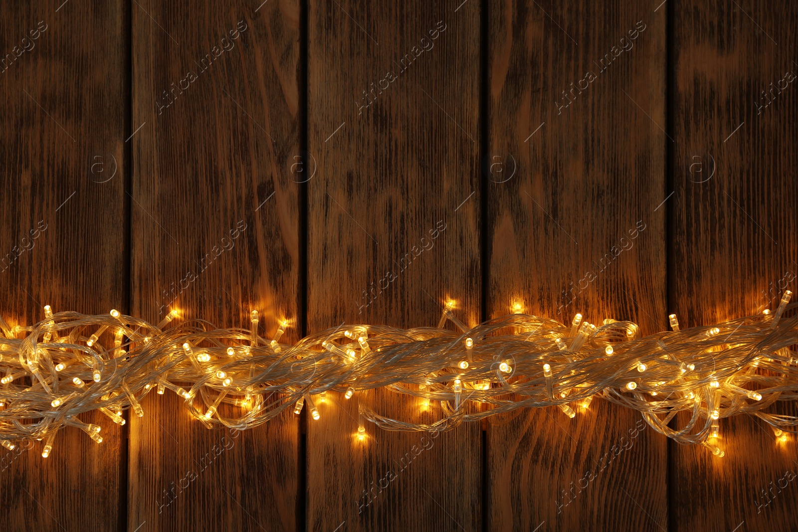 Photo of Glowing Christmas lights on wooden background, top view. Space for text