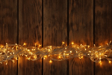 Glowing Christmas lights on wooden background, top view. Space for text