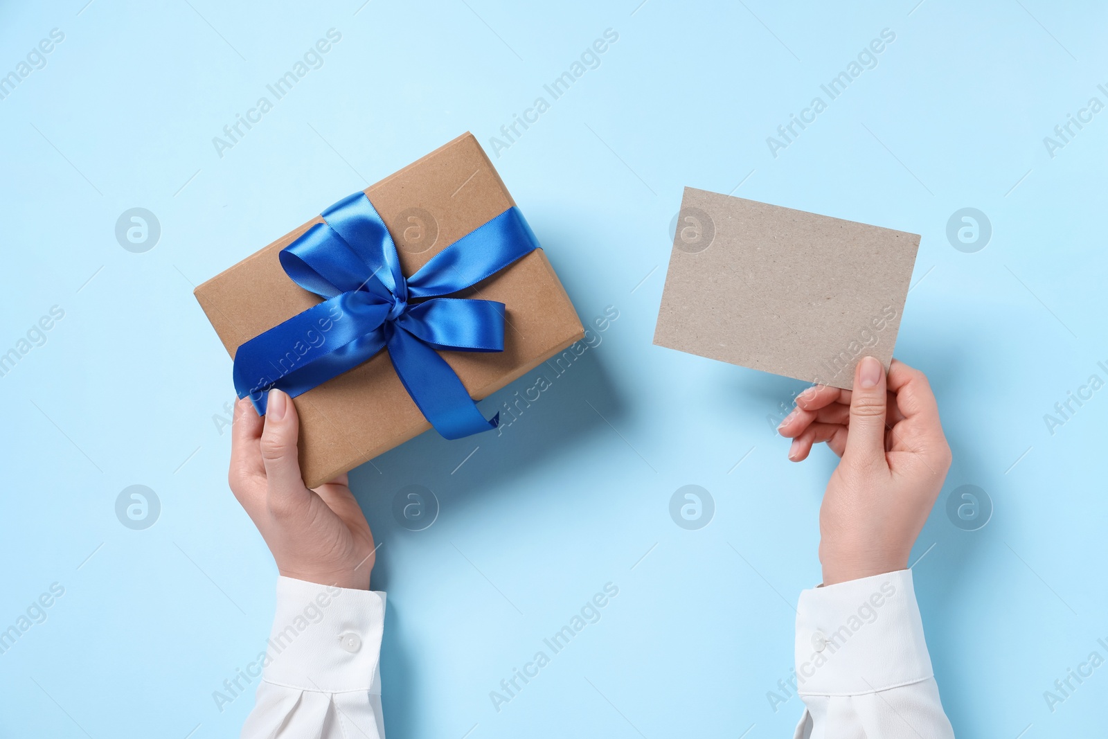 Photo of Woman holding gift box and blank card on light blue background, top view. Space for text