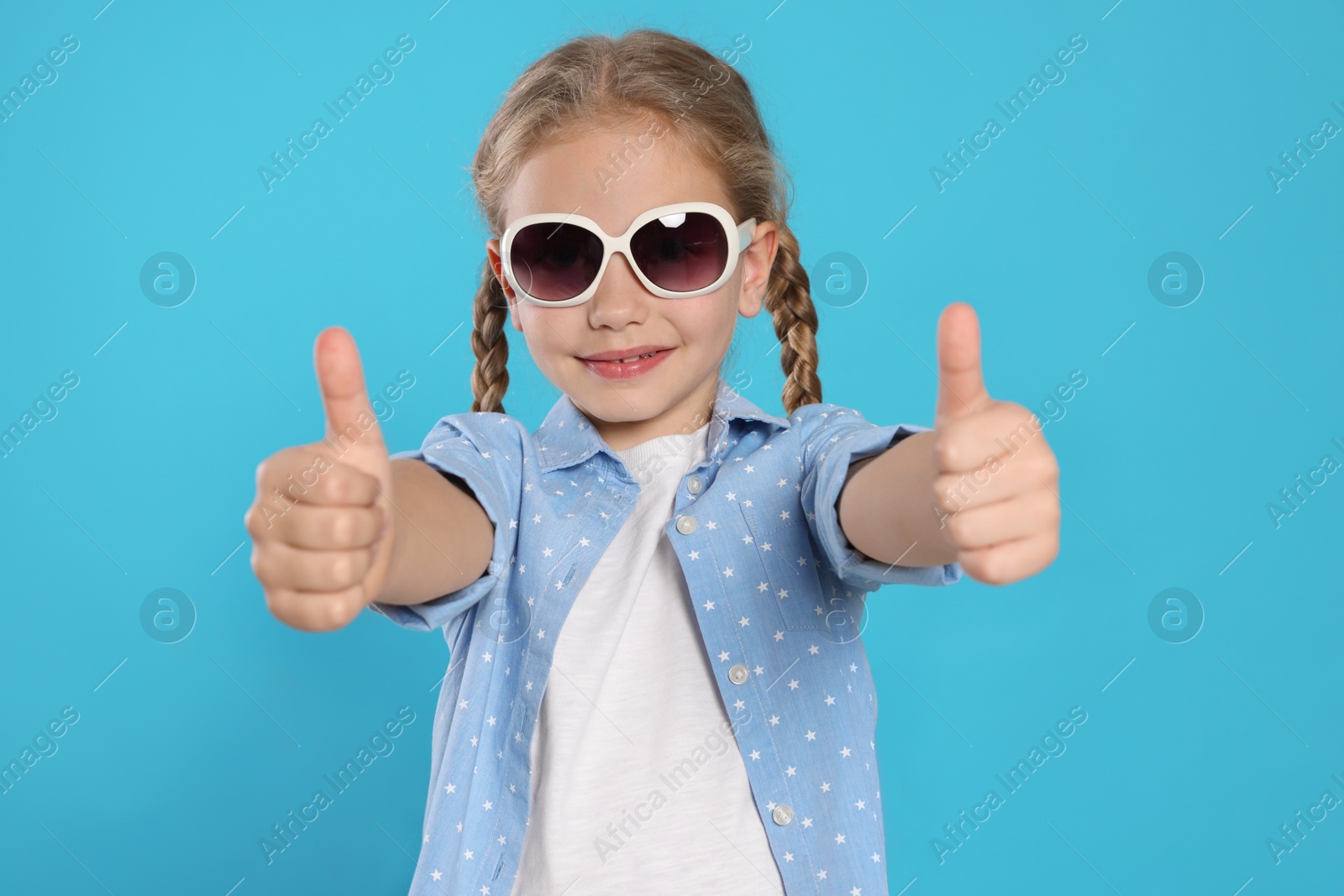 Photo of Girl in stylish sunglasses showing thumbs up on light blue background