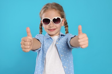 Photo of Girl in stylish sunglasses showing thumbs up on light blue background