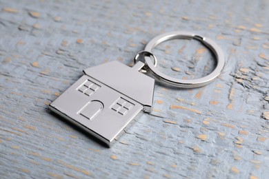 Photo of Metal keychain in shape of house on grey wooden table, closeup