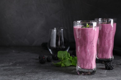 Glasses of tasty blackberry smoothie on grey table. Space for text