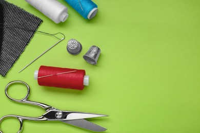 Flat lay composition with thimbles and different sewing tools on green background, space for text