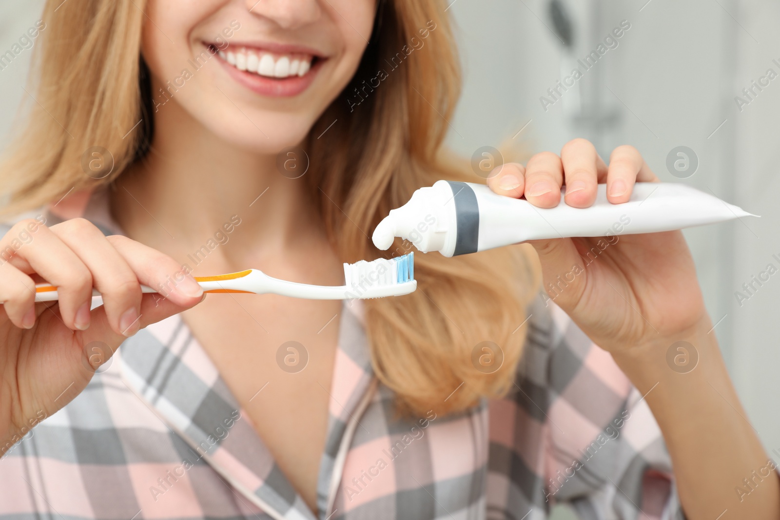 Photo of Woman applying toothpaste on brush indoors, closeup