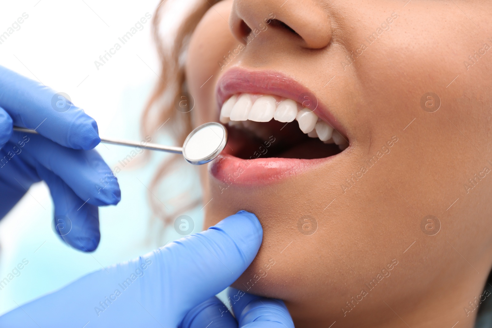 Photo of Dentist examining African-American woman's teeth with mirror, closeup