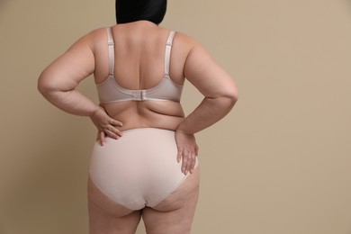 Photo of Back view of overweight woman in beautiful underwear on beige background, space for text. Plus-size model