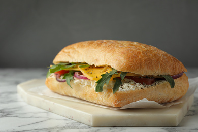 Delicious sandwich with fresh vegetables and cheese on white marble table