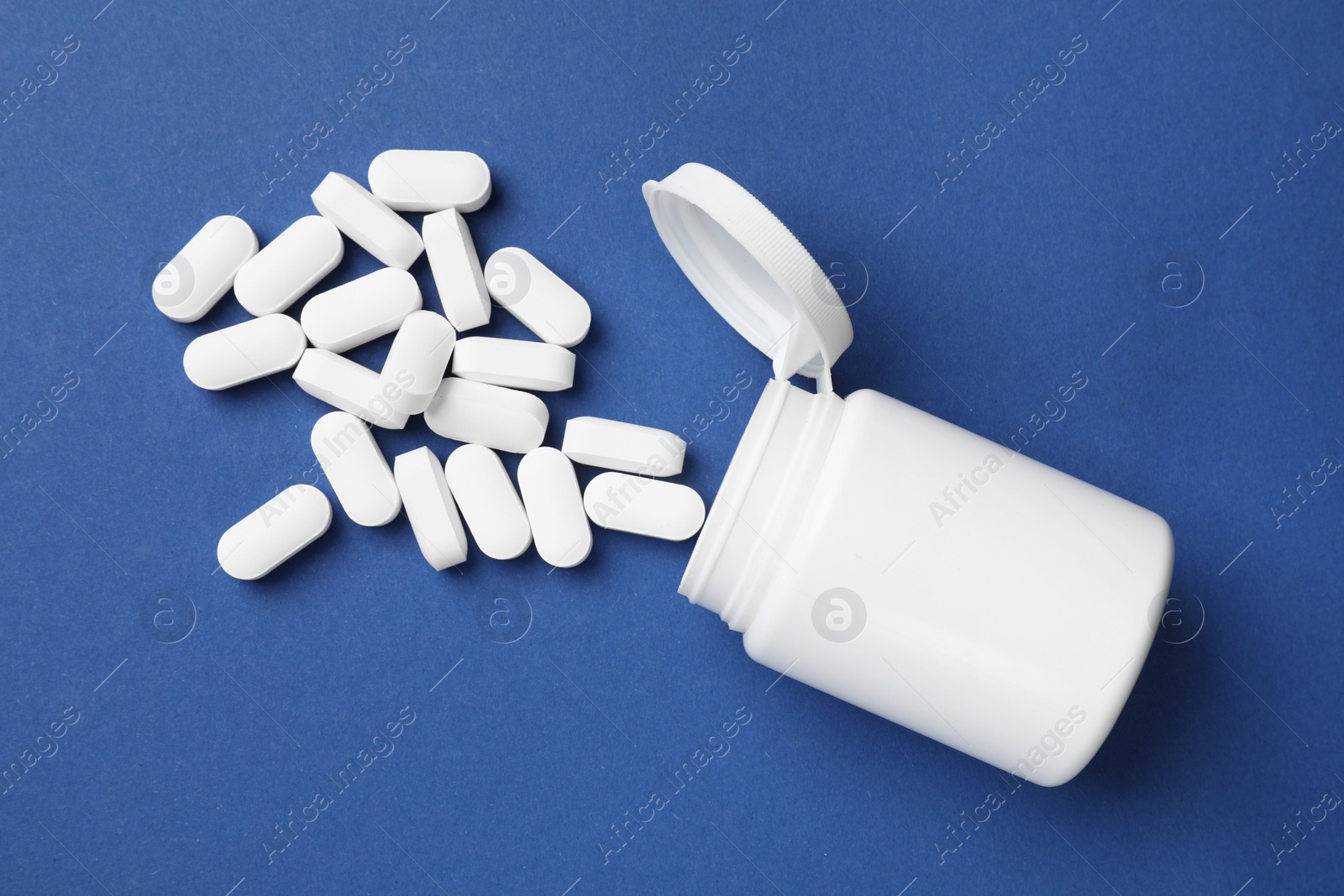 Photo of Vitamin pills and bottle on blue background, top view