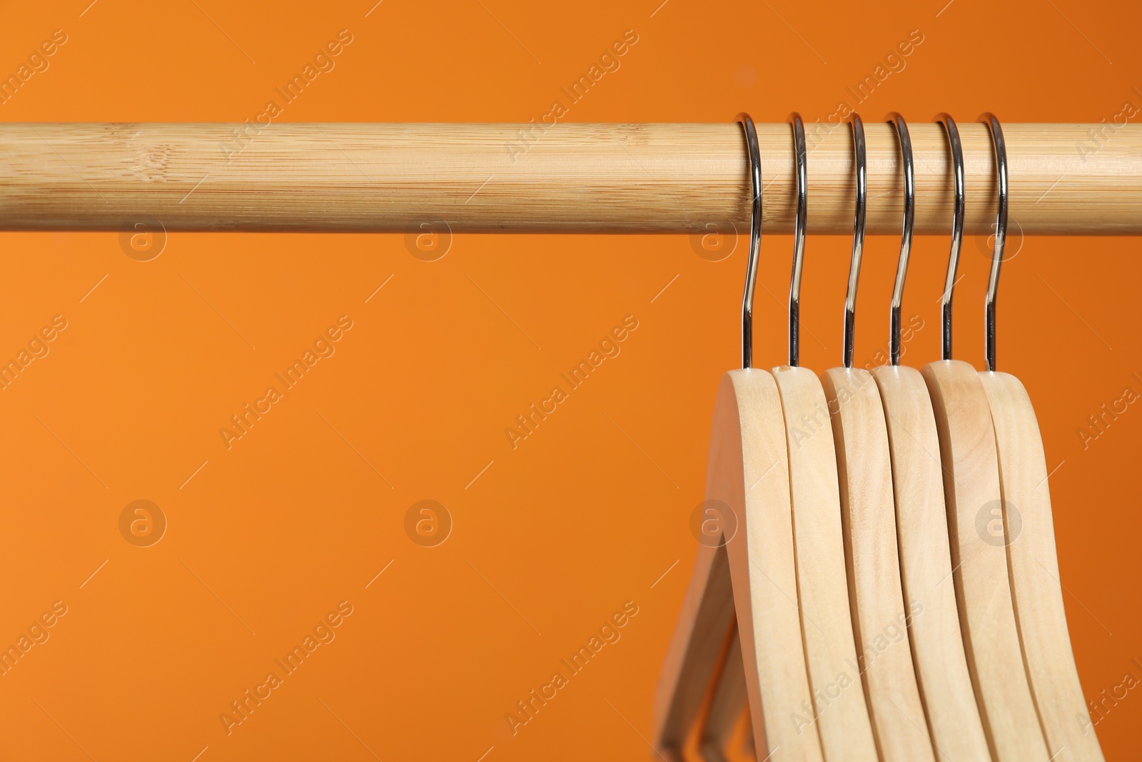 Photo of Empty clothes hangers on wooden rack against orange background, closeup. Space for text