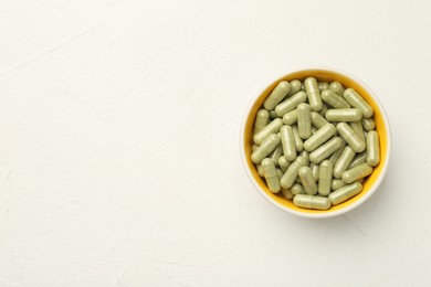 Photo of Vitamin capsules in bowl on white wooden table, top view. Space for text