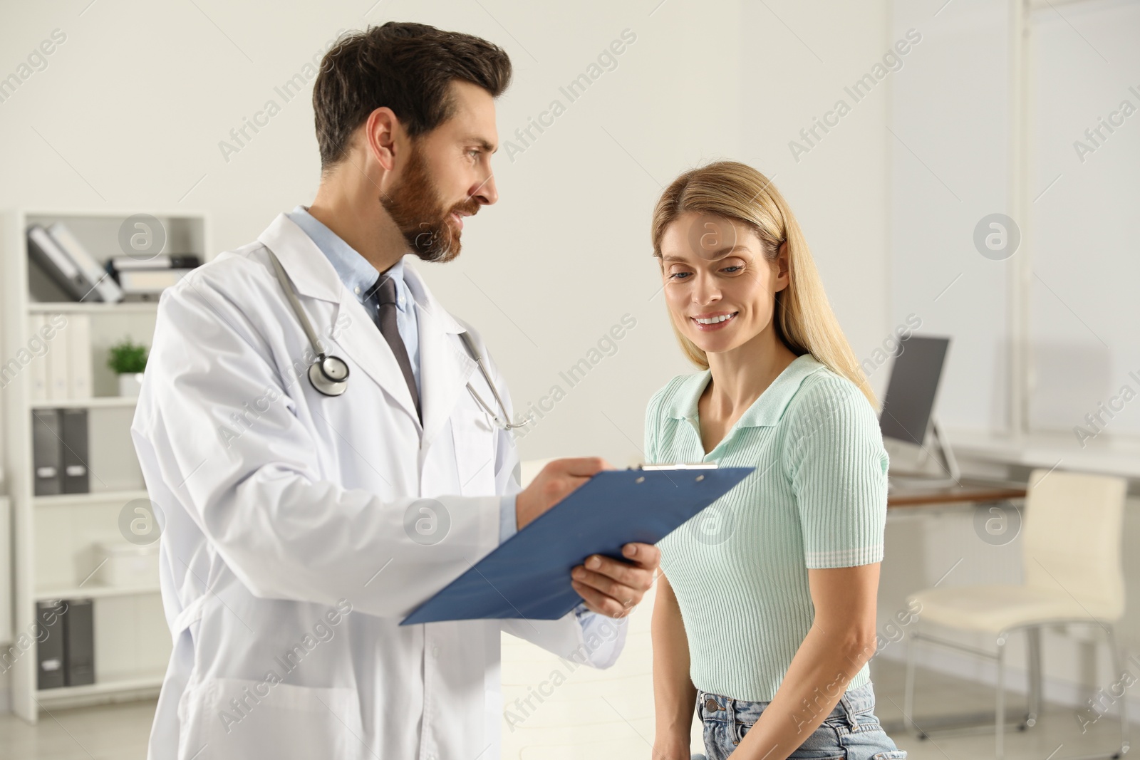 Photo of Doctor with clipboard consulting patient in clinic