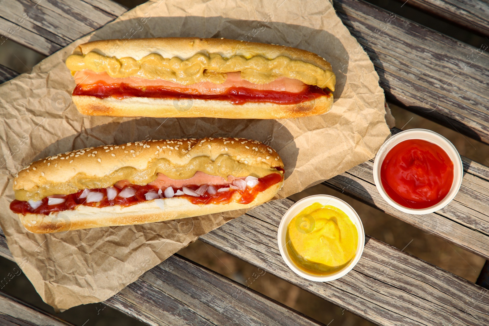 Photo of Fresh delicious hot dogs and sauces on wooden surface outdoors, flat lay