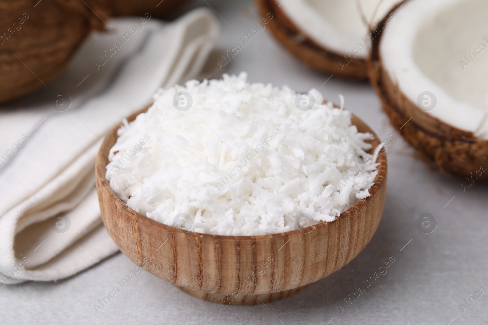 Photo of Coconut flakes in bowl and nut on light grey table, closeup