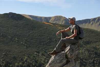 Photo of Tourist with backpack enjoying mountain landscape on rocky peak