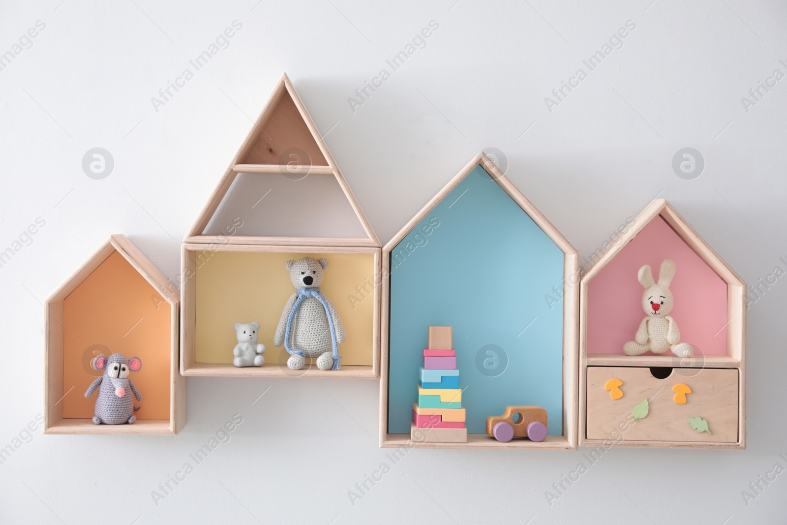 Photo of Different house shaped shelves with toys on white wall. Interior design
