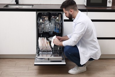 Photo of Man loading dishwasher with dirty plates indoors