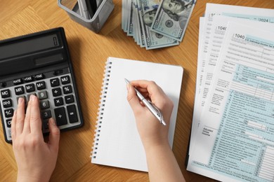 Photo of Payroll. Woman using calculator while taking notes in notebook at wooden table, top view