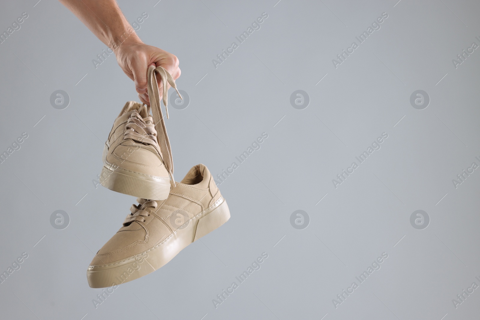 Photo of Man holding stylish sneakers on light grey background, closeup. Space for text