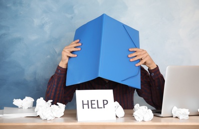 Man covering head with folder at table in office. Asking for help