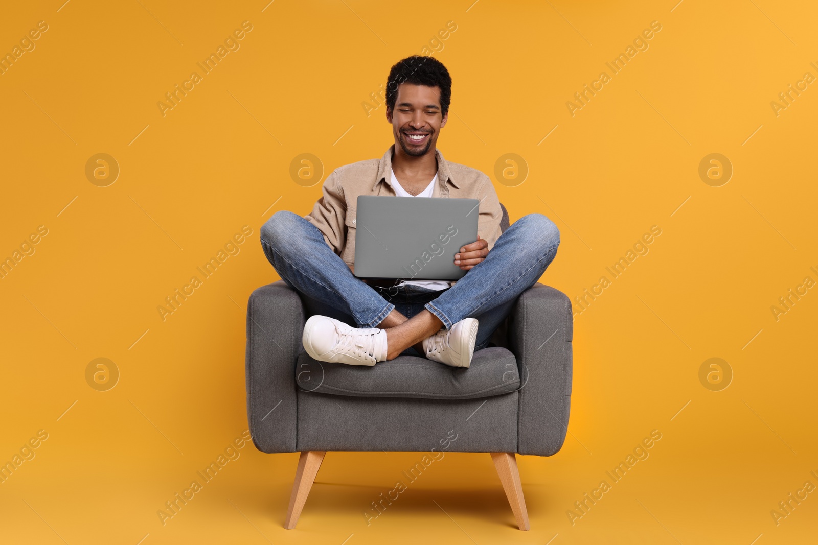 Photo of Happy man with laptop sitting in armchair on orange background