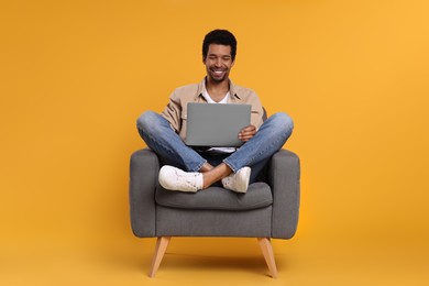 Happy man with laptop sitting in armchair on orange background