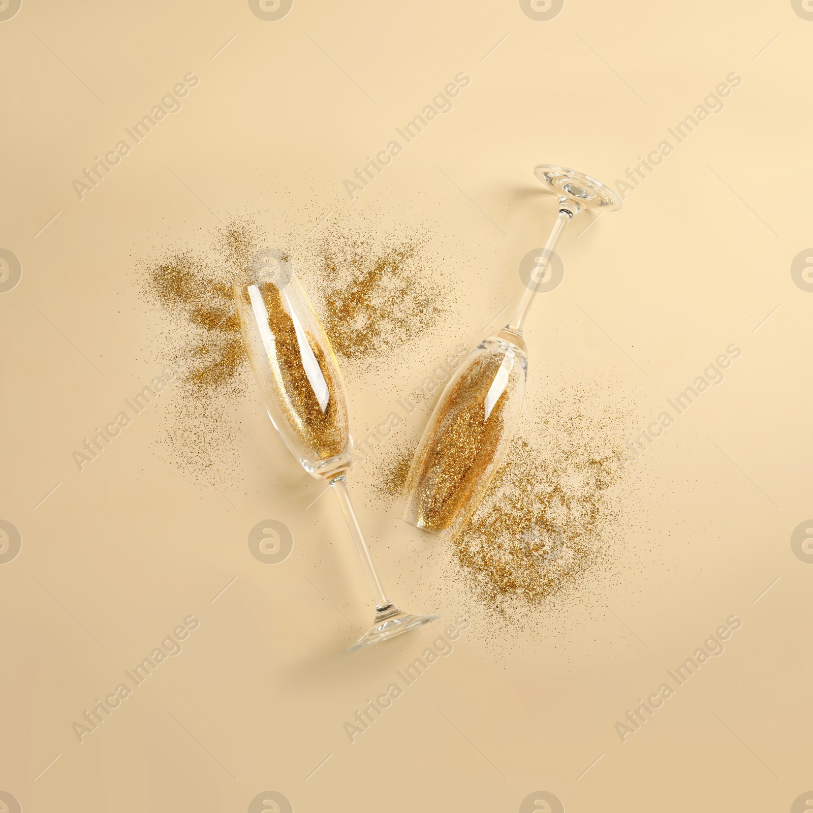 Photo of Champagne glasses with gold glitter on beige background, flat lay. Hilarious celebration