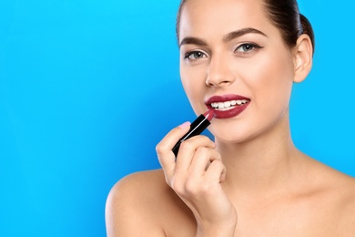 Young woman applying lipstick on color background. Space for text