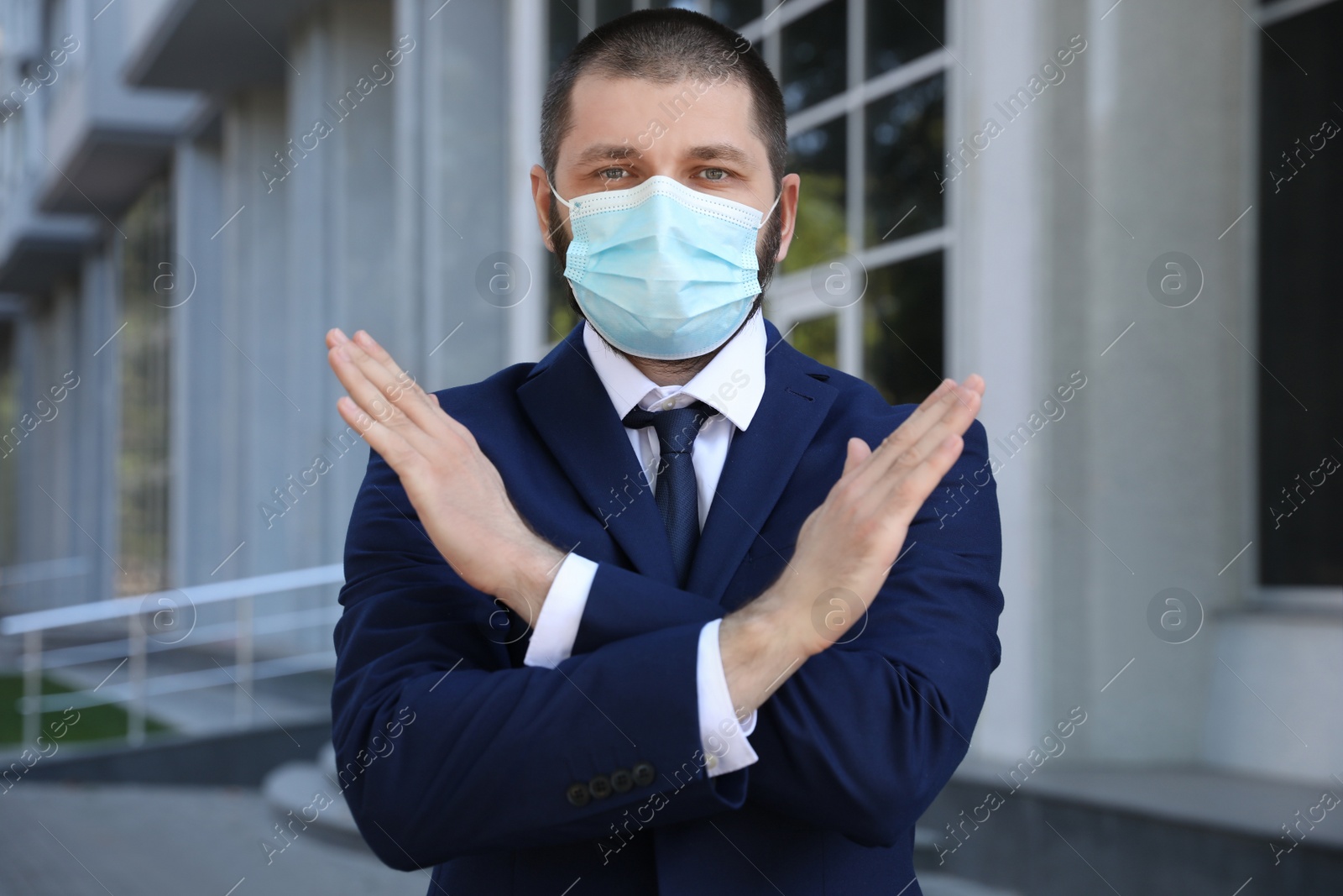 Photo of Man in protective face mask showing stop gesture outdoors. Prevent spreading of coronavirus