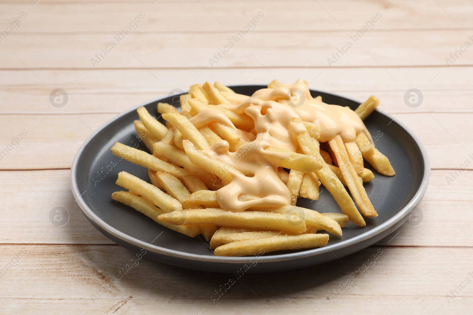 Photo of Delicious french fries with cheese sauce on wooden table