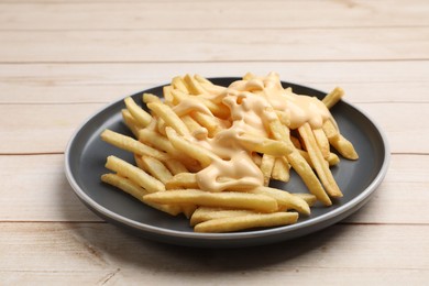 Photo of Delicious french fries with cheese sauce on wooden table