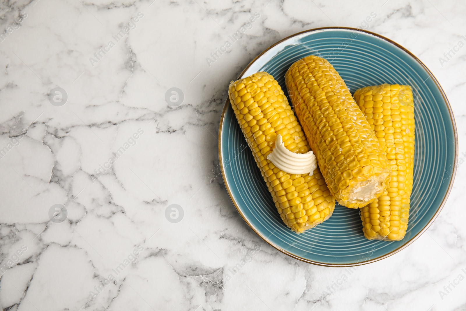 Photo of Delicious boiled corn with butter on white marble table, top view. Space for text