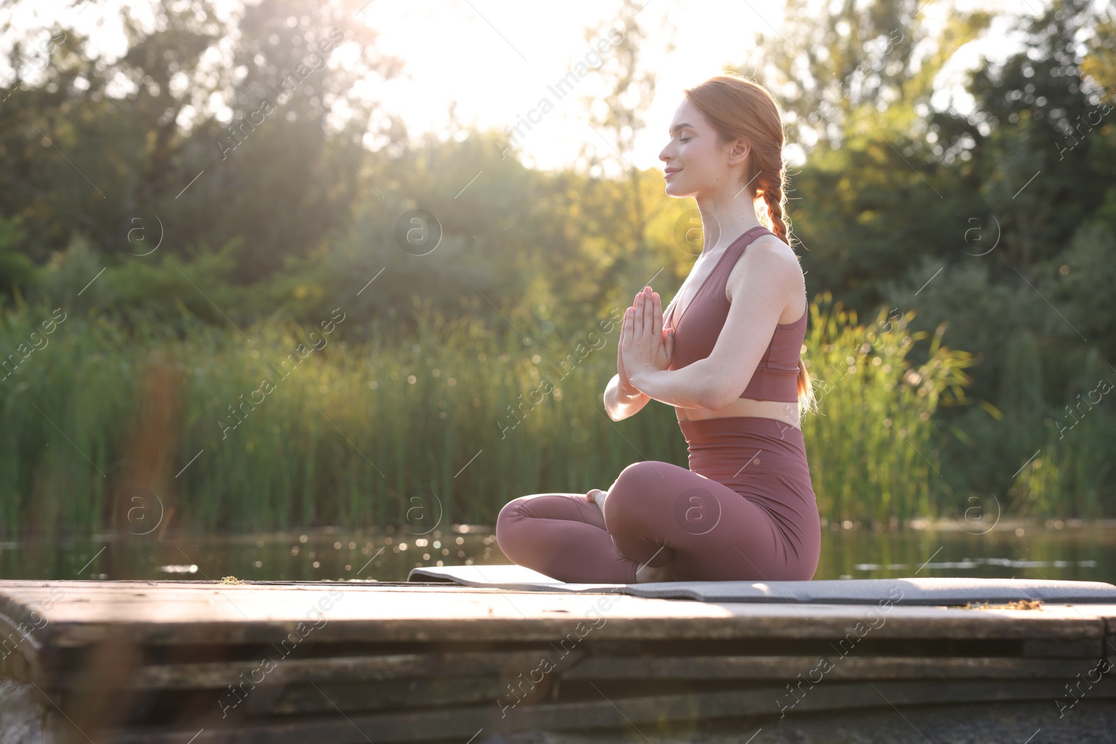 Photo of Beautiful woman practicing Padmasana on yoga mat on wooden pier near pond, space for text. Lotus pose