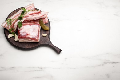 Photo of Tasty pork fatback with pickled cucumber, garlic and parsley on white marble table, top view. Space for text