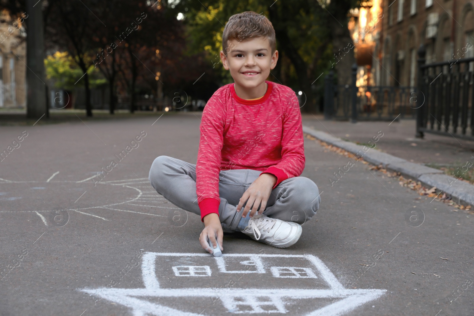Photo of Child drawing house with chalk on asphalt